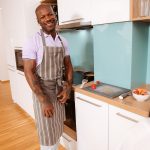 bald headed black man wearing apron cooks meal