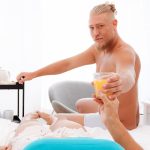 Blonde male actor hands woman a glass of orange juice.